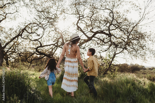 Back view of mother holding son and daughter's hands and walking photo