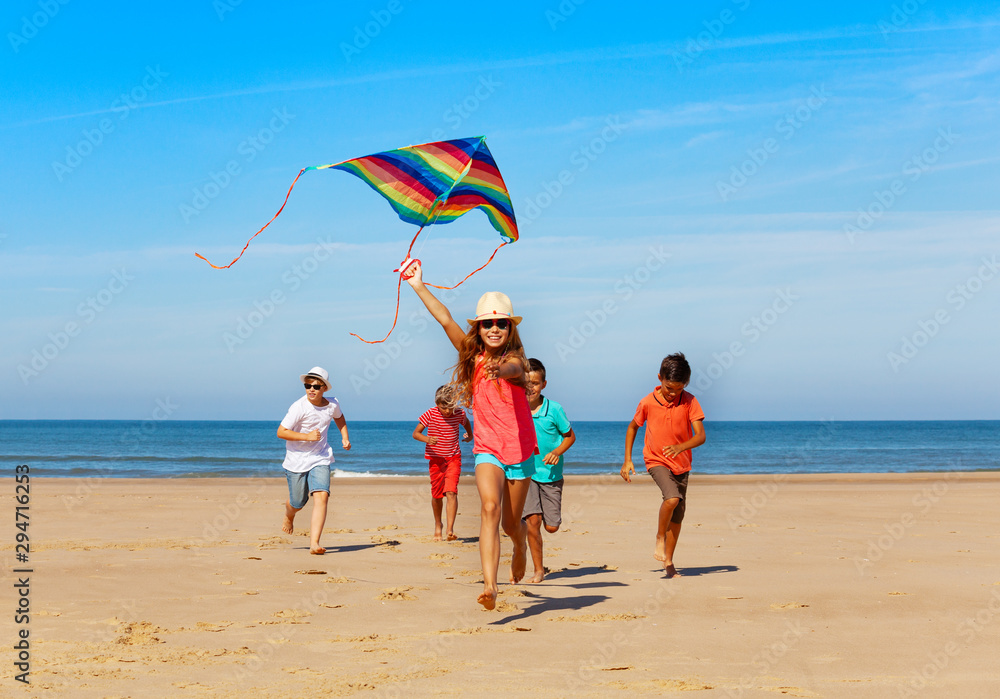 Group of happy kids run with kite on the beach