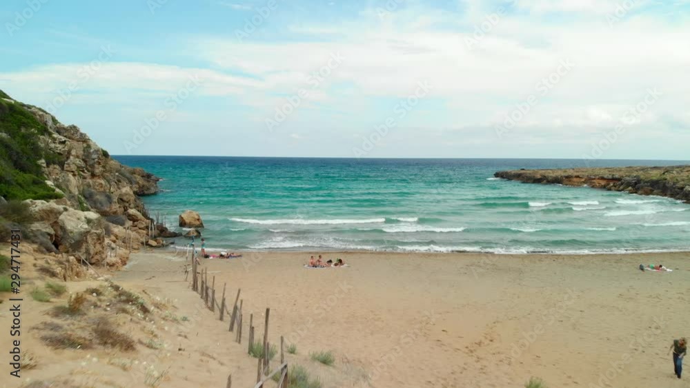 AERIAL: Man walking on the beach towards the sea, in Calamosche Vendicari Reserve, a small paradise in Sicily Italy AERIAL: Man walking on the beach towards the sea, in Calamosche Vendicari Reserve, a small paradise in Sicily Italy