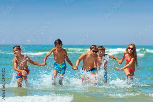 Many kids hold hands and run in the ocean water