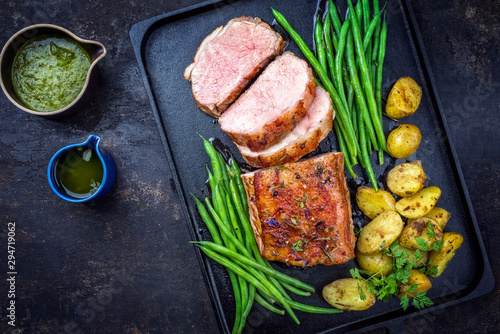 Traditional roasted dry aged veal tenderloin with beans and potatoes offered as top view on a modern design cast iron tray photo