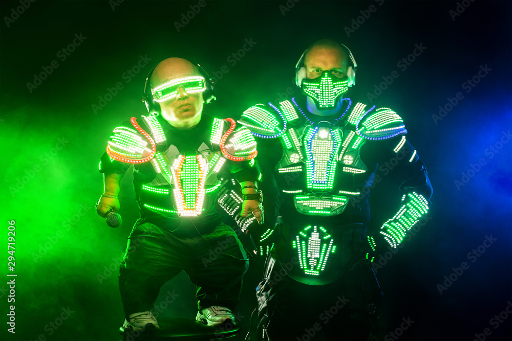 Mysterious man and midget in black wear, neon mask and gloves. Character pastors or wizards in robe from the future. Assassin with strong face expression. Fantasy book or computer game cover concept.