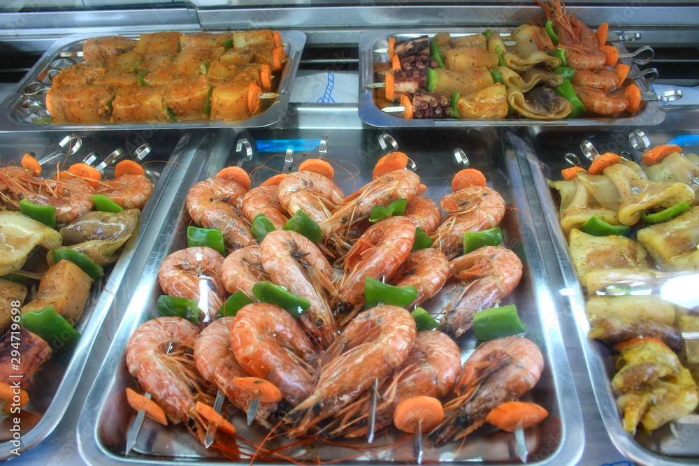 Giant shrimps prepared for grilling, in the background skewers of different species of fish