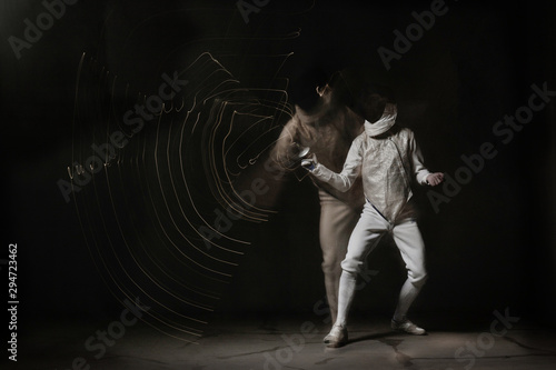 Fototapeta Naklejka Na Ścianę i Meble -  Fencer in white outfit is performing fight. Multi Exposure, freeze light, dark background 