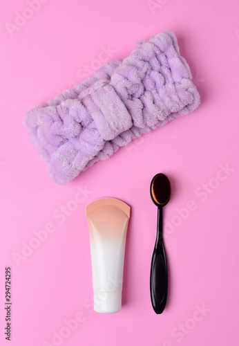 Cosmetics and accessories on a pink background. flat lay. Black makeup brush, foundation and purple headband on a pink background.