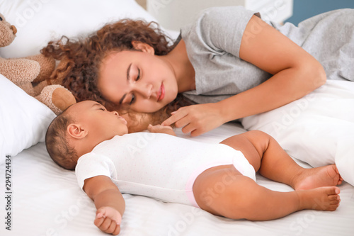 Young African-American woman and her baby sleeping on bed