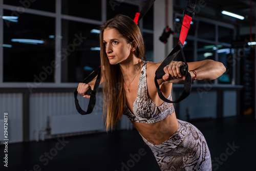 Beautiful young sportswoman is doing exercises with equipment. A woman in the gym for circular training is engaged in loops TRX. Athlete Making Functional workout With Suspension Cable. straps system.