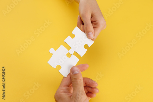 cropped view of woman and man matching pieces of white puzzle on yellow background photo