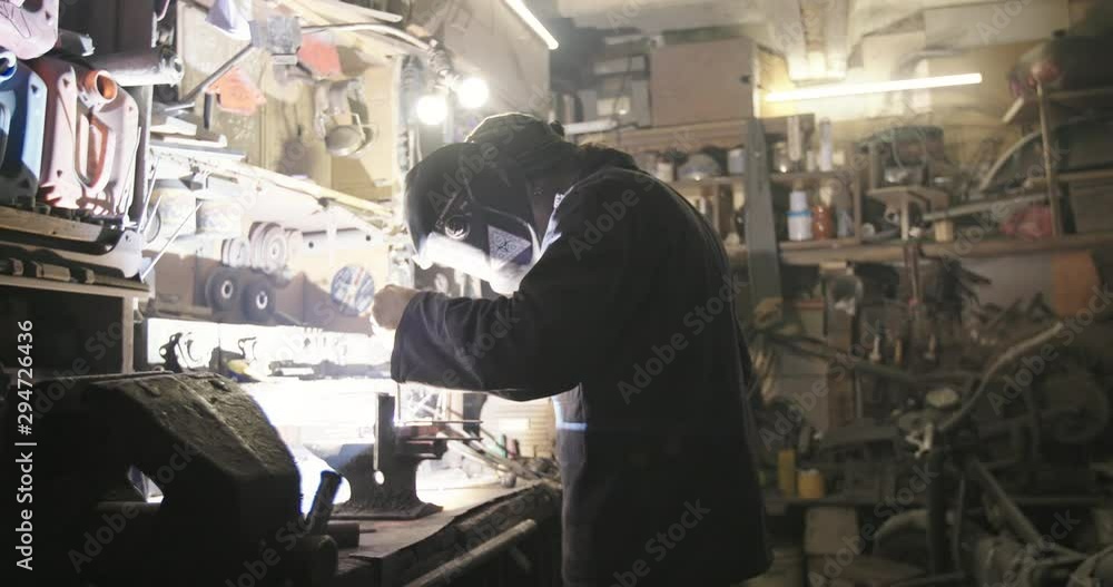 Real mechanic welds a part in an old dark garage. Real mechanic welds a part in an old dark garage.