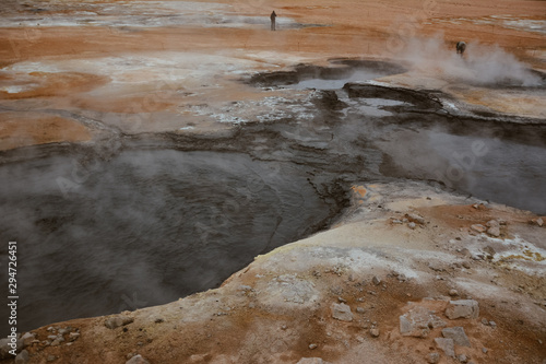 Boiling mudpots in the geothermal area Hverir and cracked ground around with unrecognisable tourists, Iceland in summer. Myvatn region, North part of Iceland