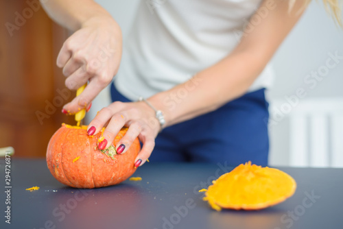 A woman carves her face on a pumpkin for a Halloween lamp on a black table. Close-up female hands making Jack-o'-lantern to the eve of all saints..