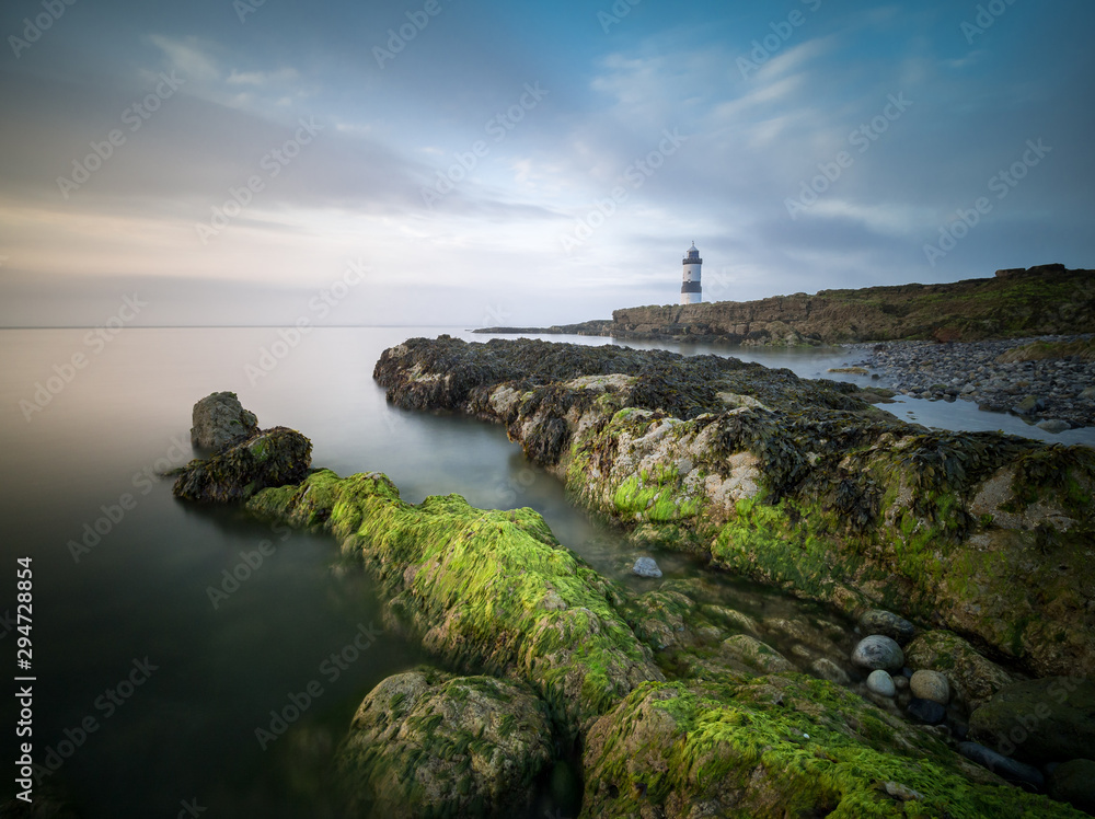 A lighthouse with algae covered rocks in the foreground