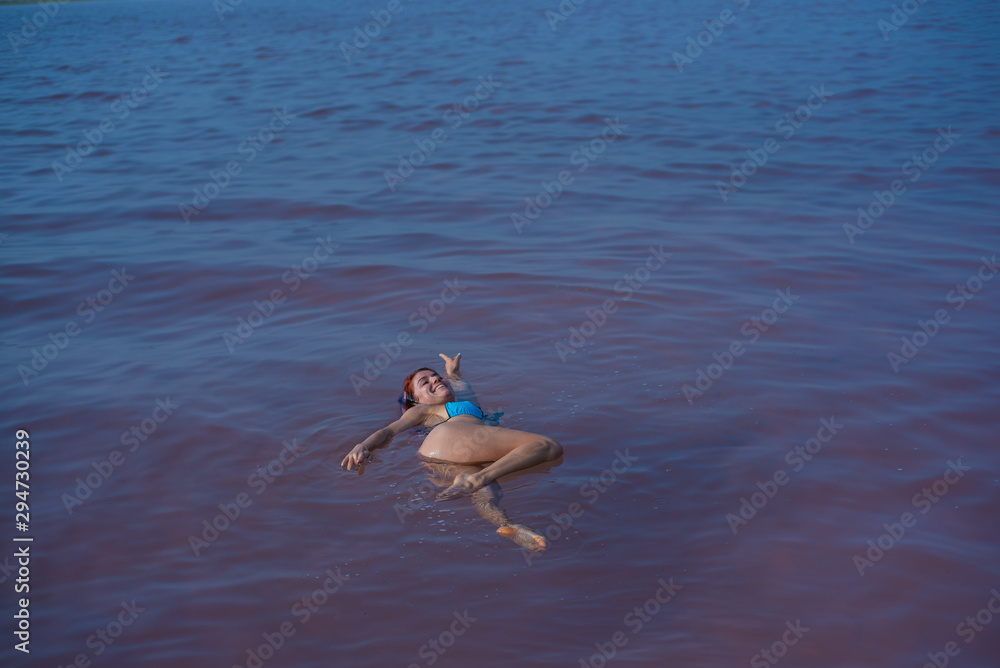 A woman in a blue bikini swims on her back in a salt lake. Miracle of nature pink lake. Deposit and extraction of salt. Dense water pushing to the surface. Therapeutic procedures in mineral water.