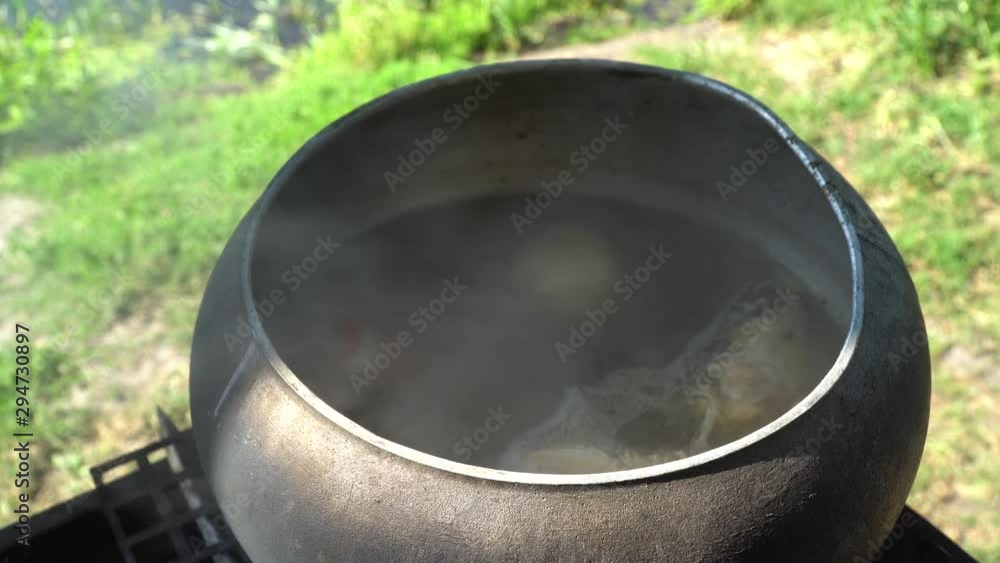 Iron cast cauldron boiling ear over open log fire Iron cast cauldron boiling ear over open log fire
