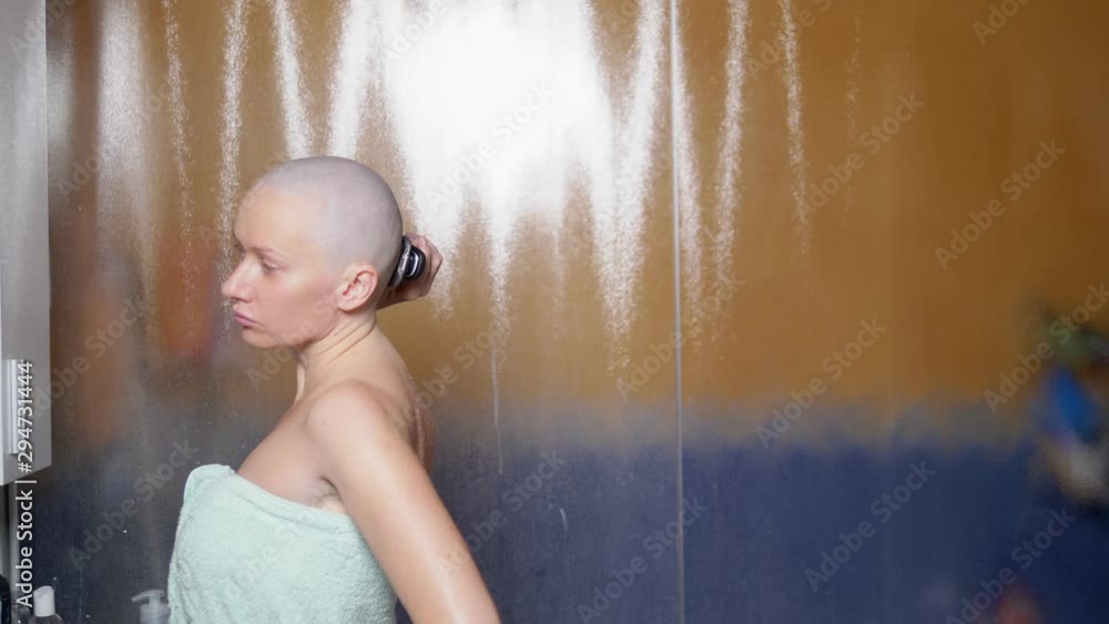 a bald woman shaves her head in the bathroom after a shower. Copy space ...