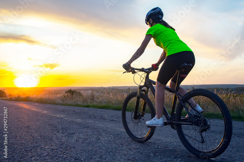 Beautiful girl cyclist rides a bicycle on the road in the sunset. Healthy lifestyle and sport. Leisure and hobbies