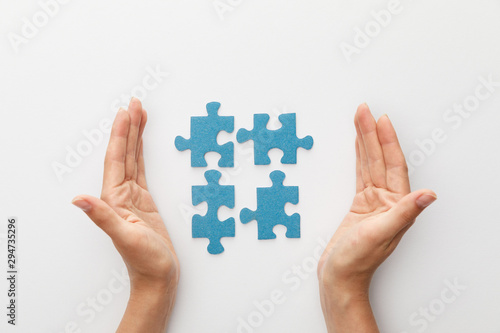 cropped view of woman hands near pieces of blue jigsaw puzzle on white background