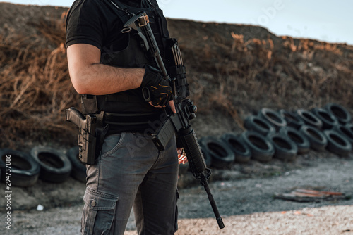 Image of armed man with rifle and gun standing outdoors, close-up.
