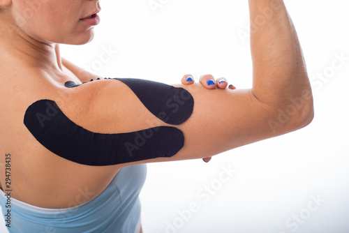 Female shoulder with kineziotape on a white background. Alternative medicine for sports injuries of joints and ligaments. Young sportswoman with a black Medical taping on a sore shoulder. Close up. photo