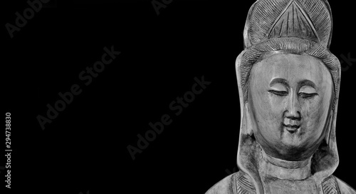 Buddhist religion and meditation. Kannon or Guanyin, the Goddess of Mercy, wooden statuette on black background (Black and White with copy space)