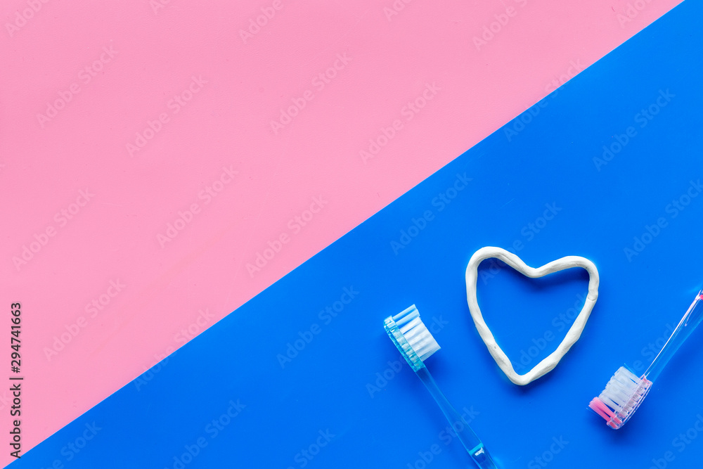 Teeth care. Heart drawn with toothpaste near toothbrushes on pink and blue background top view copy space Teeth care. Heart drawn with toothpaste near toothbrushes on pink and blue background top view copy space