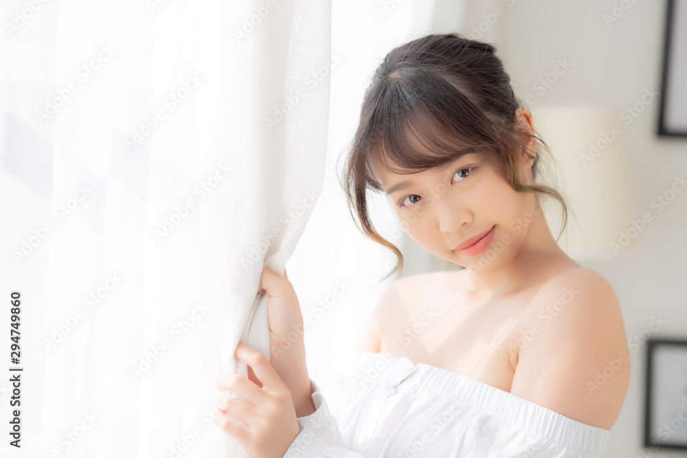 Portrait of beautiful young asian woman standing the window and smile while wake up with sunrise at morning, girl happy with freshness and cheerful, lifestyle and relax concept. Portrait of beautiful young asian woman standing the window and smile while wake up with sunrise at morning, girl happy with freshness and cheerful, lifestyle and relax concept.