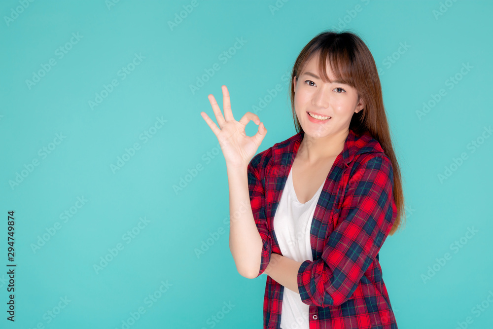 Fototapeta premium Beautiful portrait young asian woman smiling confident and excited summer holiday isolated blue background, beauty asia model girl gesture ok and cheerful success with journey, travel concept.