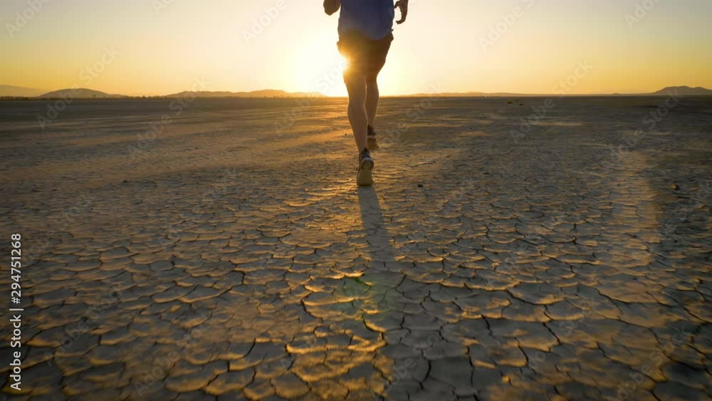 Athletic man working out with battle ropes on a dry lake at sunset