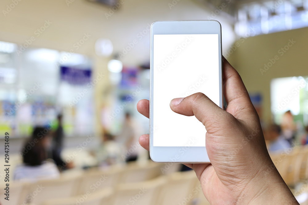Hand of a man holding smartphone device on blur hospital background. Hand of a man holding smartphone device on blur hospital background.