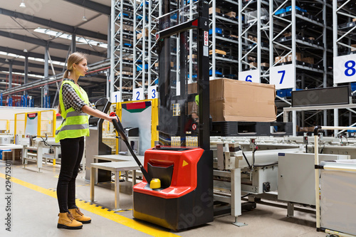 Storehouse employee in uniform working on forklift in modern automatic warehouse.Boxes are on the shelves of the warehouse. Warehousing, machinery concept. Logistics in stock. photo