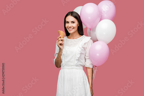 smiling girl in dress holding balloons and ice cream cone isolated on pink © LIGHTFIELD STUDIOS