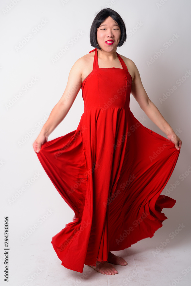 Full body shot of happy young gay Asian man holding dress
