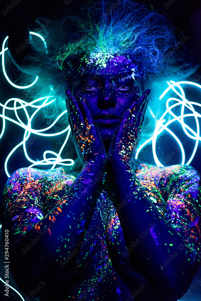 The girl is the image of the devil, contact lenses and with horns. Woman in  UV paint. fluorescent powder. Body art glowing in ultraviolet light. Stars  in the eyes. Stock Photo