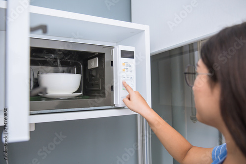 women reheat food by using microwave oven with glass ceramic bowl.