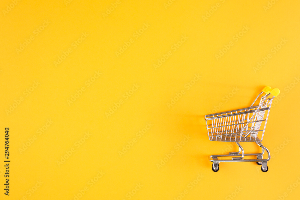 Shopaholic. Buyer. Shopping concept. Close-up. Isolated shopping trolley on a yellow background. Copy space. - obrazy, fototapety, plakaty 