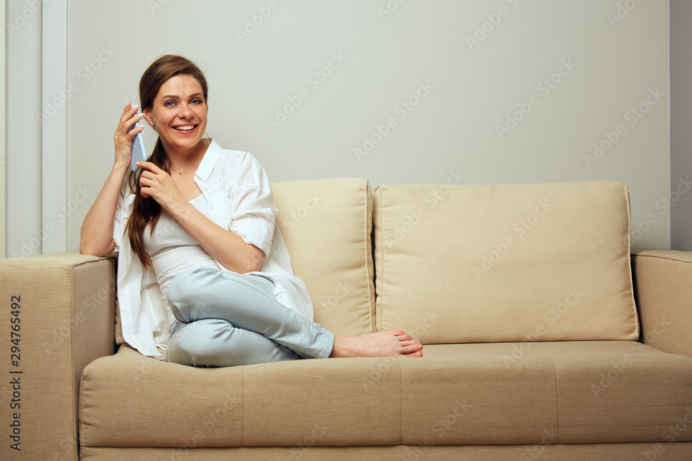 Smiling woman sitting on sofa at home using smartphone. Smiling woman sitting on sofa at home using smartphone.