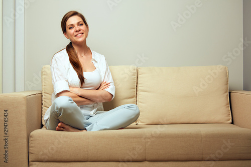 Happy woman sitting on sofa at home with crossed legs.