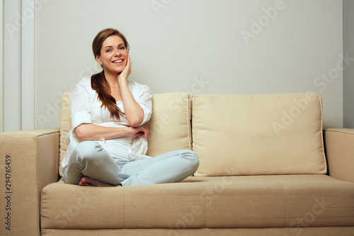 Happy woman sitting on sofa at home with crossed legs.