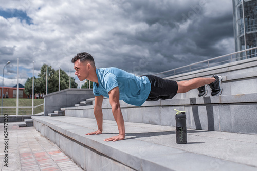 male athlete does push-ups lying down, in spring in spring city stands at bar, an exercise on abdominal muscles. Active lifestyle, workout, fitness in fresh air. Motivation for sports.