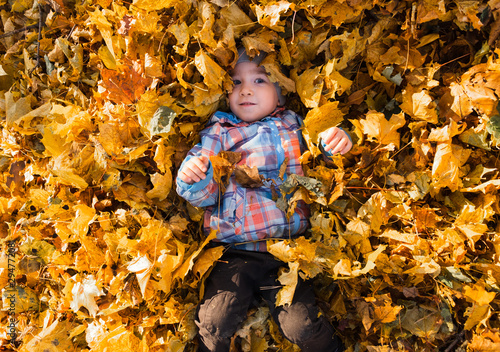 Little happy child playing with autumn leaves in the forest. The boy lies among the fallen leaves.