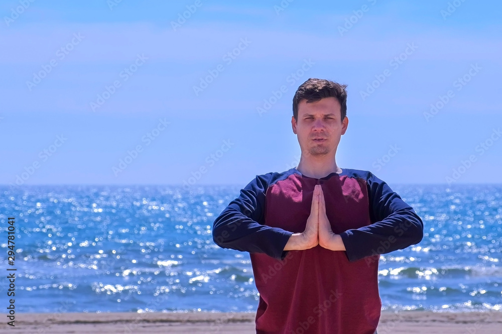 Yoga training on the beach. Portrait of young man is meditating on the sea beach putting hands in namaste pose. Outdoor sport activity. Yoga training on the beach. Portrait of young man is meditating on the sea beach putting hands in namaste pose. Outdoor sport activity.