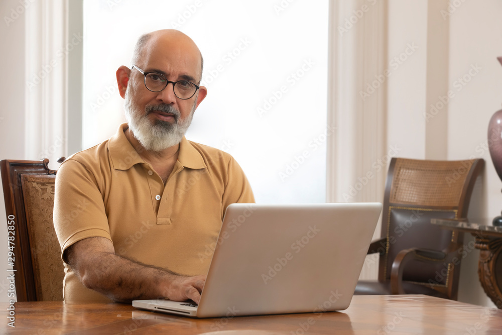 An old man sitting at the dining table with his laptop. (Senior) An old man sitting at the dining table with his laptop. (Senior)
