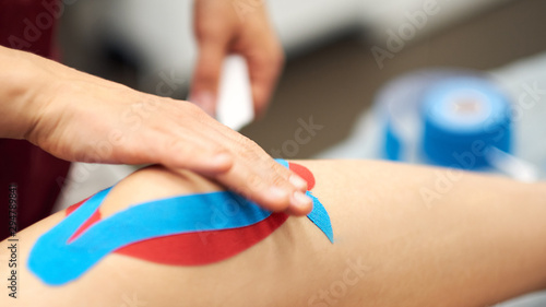 Sports injury kinesio treatment. therapist placing kinesio tape on patient s knee