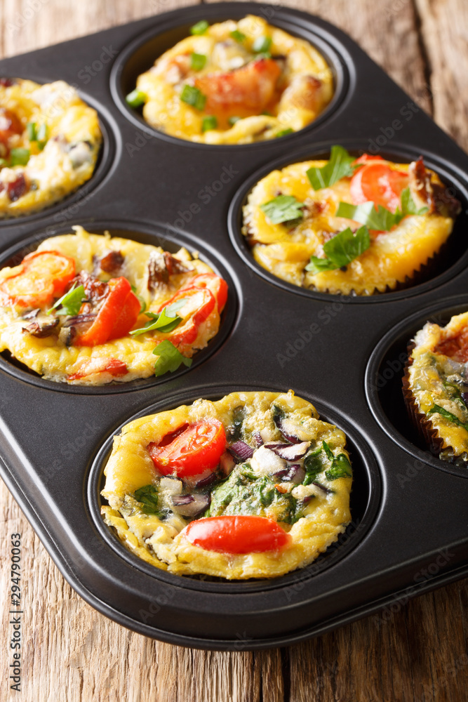 Tasty hot egg muffins with bacon, tomatoes, spinach and mushrooms close-up in a baking dish. vertical