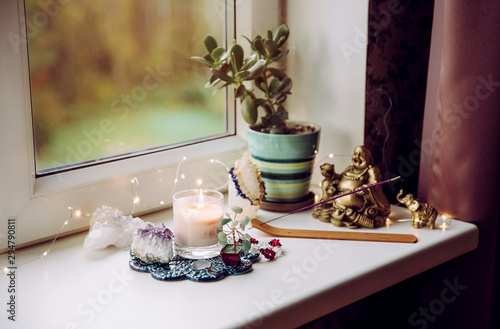 Feng Shui altar at home in living room or bed room. Attracting wealth and prosperity concept. Crystal clusters, wire tree with gemstones, golden smiling Buddha figure on table window sill. 