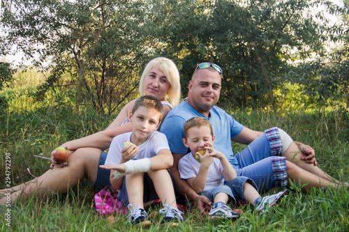 Bild auf Leinwand Happy parents of two boys relax in nature and eat apples