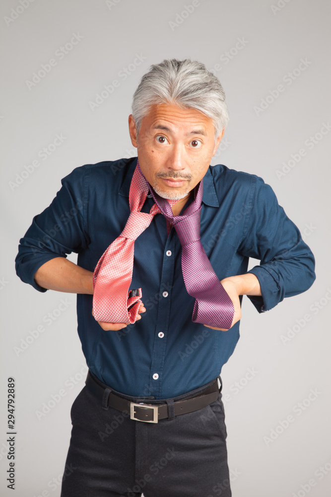 Hombre de mediana edad de origen japonés, seleccionando una corbata, dudando que corbata ponerse Hombre de mediana edad de origen japonés, seleccionando una corbata, dudando que corbata ponerse