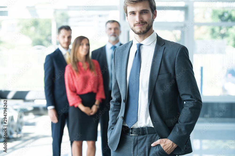 Team leader stands with coworkers in background Team leader stands with coworkers in background