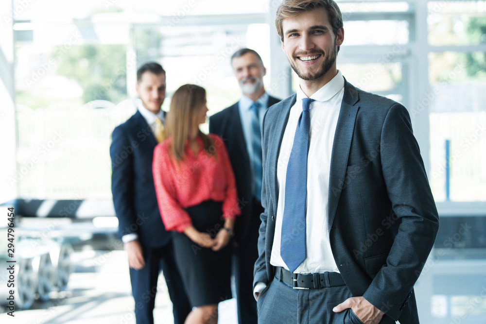Team leader stands with coworkers in background Team leader stands with coworkers in background