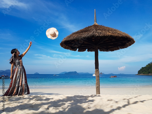 Woman in summer dress is relaxing by throwing her white hat on white sand beach and blue sky. Taken at Nyaung Oo phee Island, Myanmar. photo